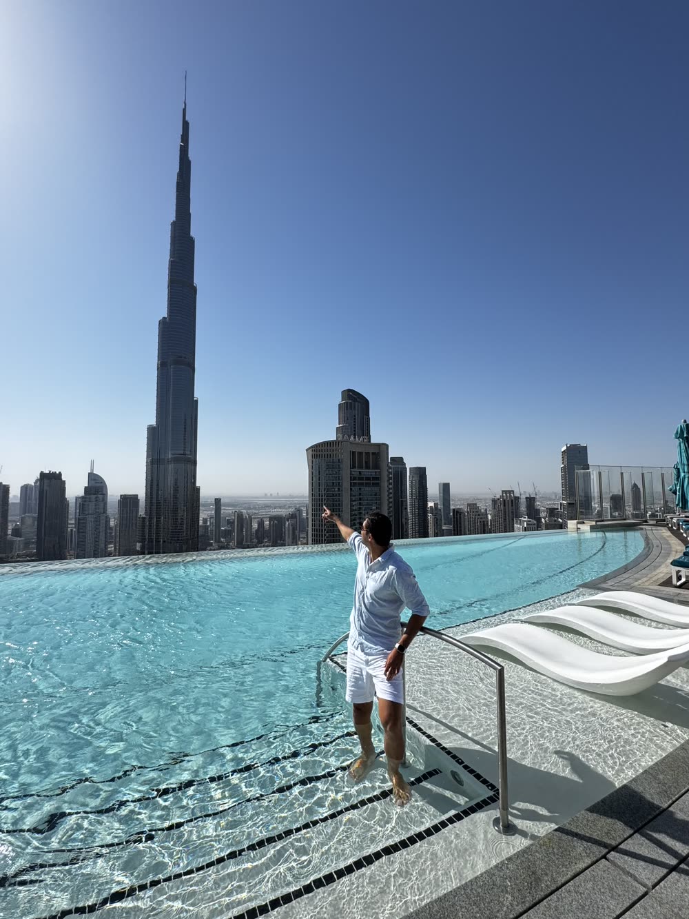 Vinicius Almeida em uma piscina de borda infinita em Dubai, apontando para o Burj Khalifa